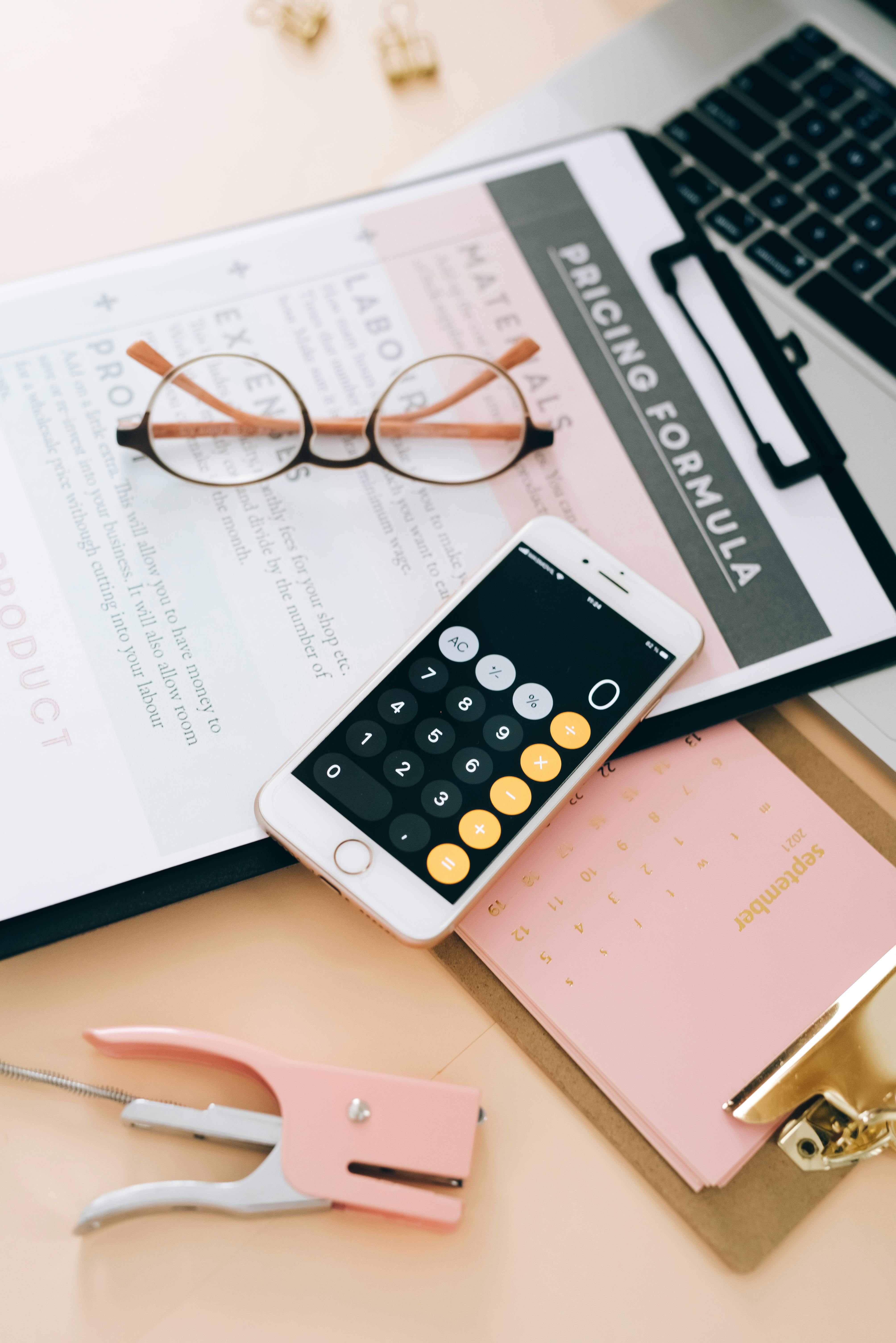 pricing formula sheet on clipboard with calculator and a pair of glasses.