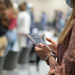 a person holding a phone standing in line. You don't see anyone's faces